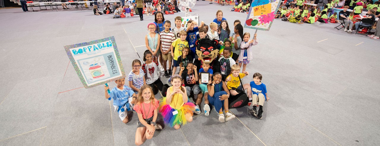wide shot of students holding signs and seated in a large room
