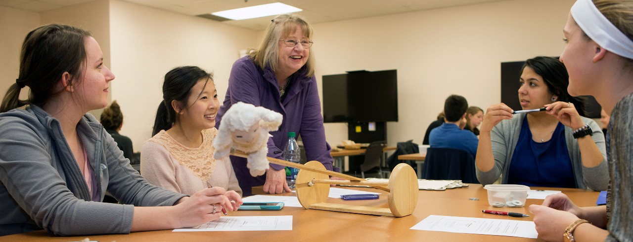 students and faculty member smiling at a plush toy