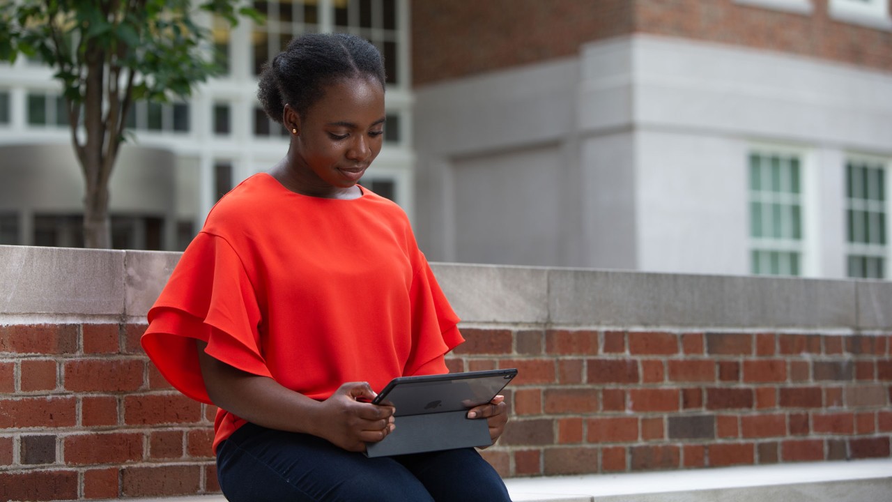 woman sits outside reading from a tablet