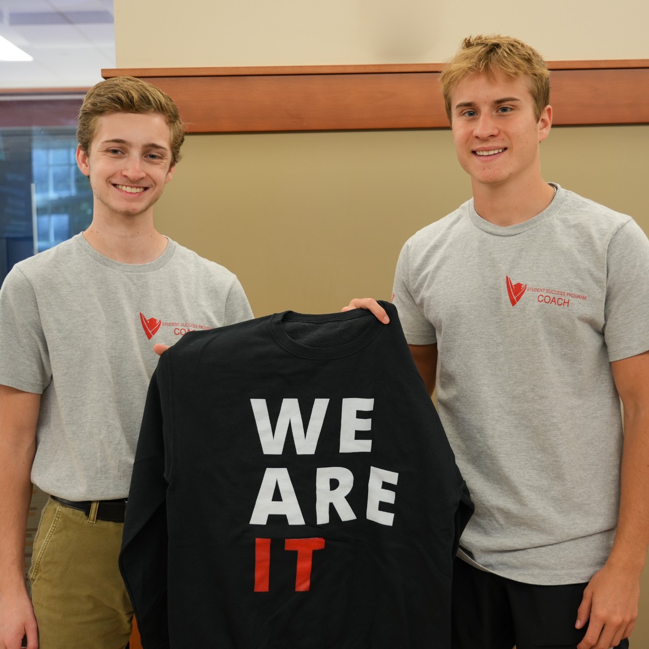 Two students holding a We Are IT sweatshirt